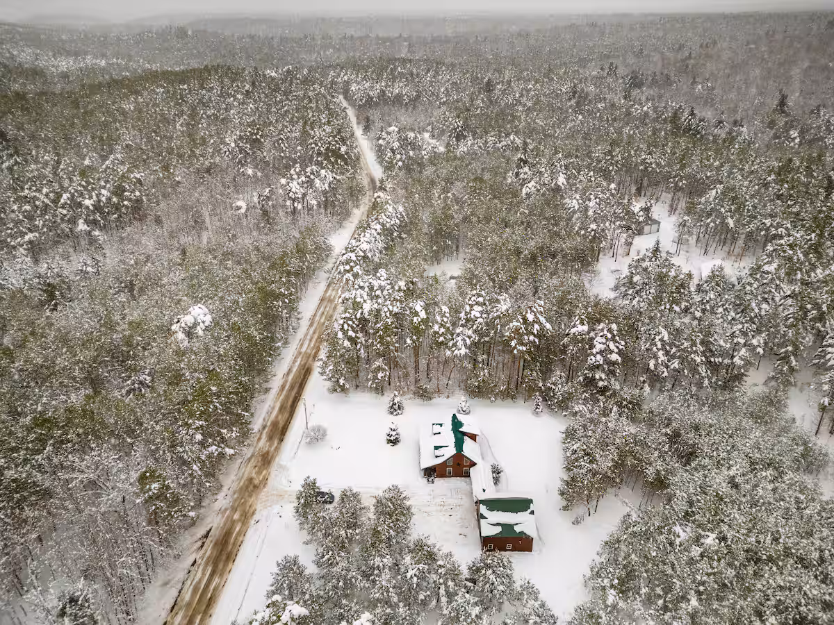 Aerial winter view of Cabin in the Pines and its detached garage, tucked into the snow-covered woods with the trail road leading up to the property