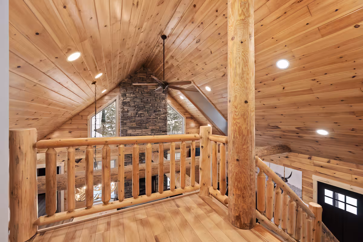 View from the upstairs loft railing down over the vaulted great room, stone fireplace chimney, and triangular window