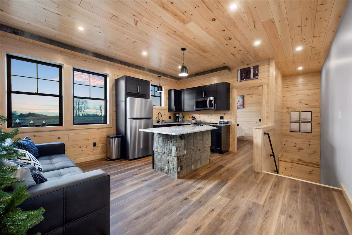 Open kitchen and living area with black cabinetry, a stone-clad island, and windows looking out over open fields