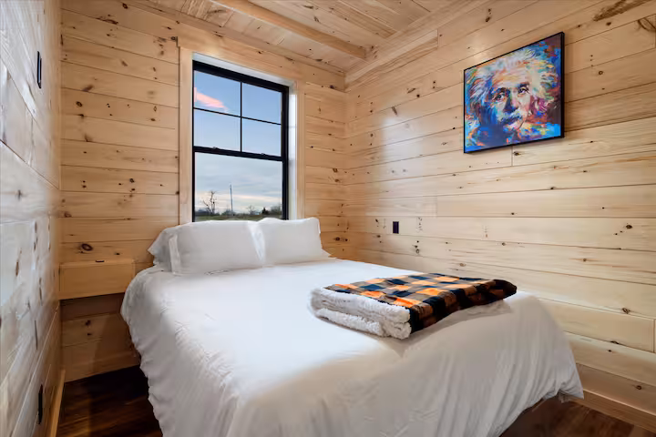 Queen bedroom finished in pine with a window and colorful framed art