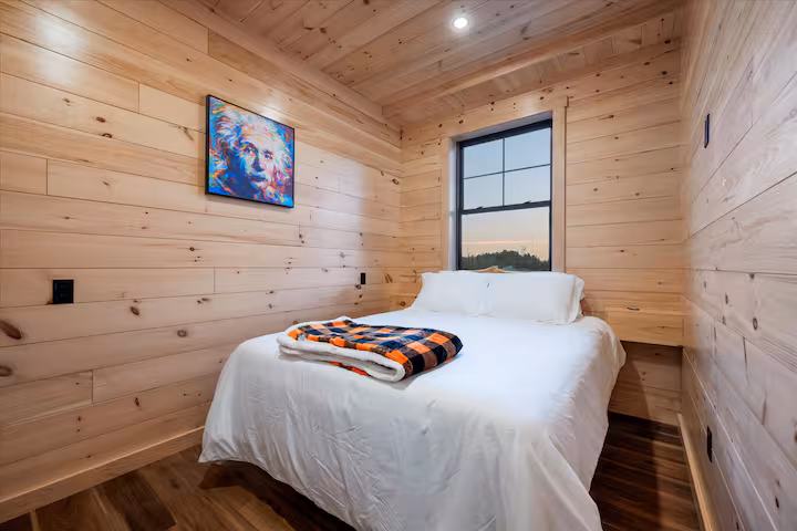 Queen bedroom finished in pine with a colorful framed art print and a window