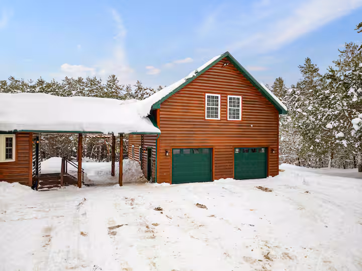 Exterior of the two-stall garage with the loft above it, log siding and green trim, snow on the ground
