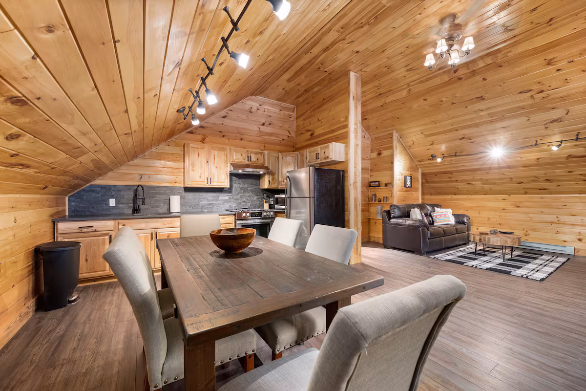 Open-plan loft interior with a dining table, full kitchen, and leather sofa under a vaulted pine ceiling