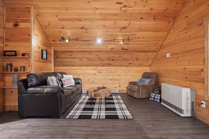 Living area with a leather sofa, recliner, and a live-edge coffee table beneath the sloped pine ceiling
