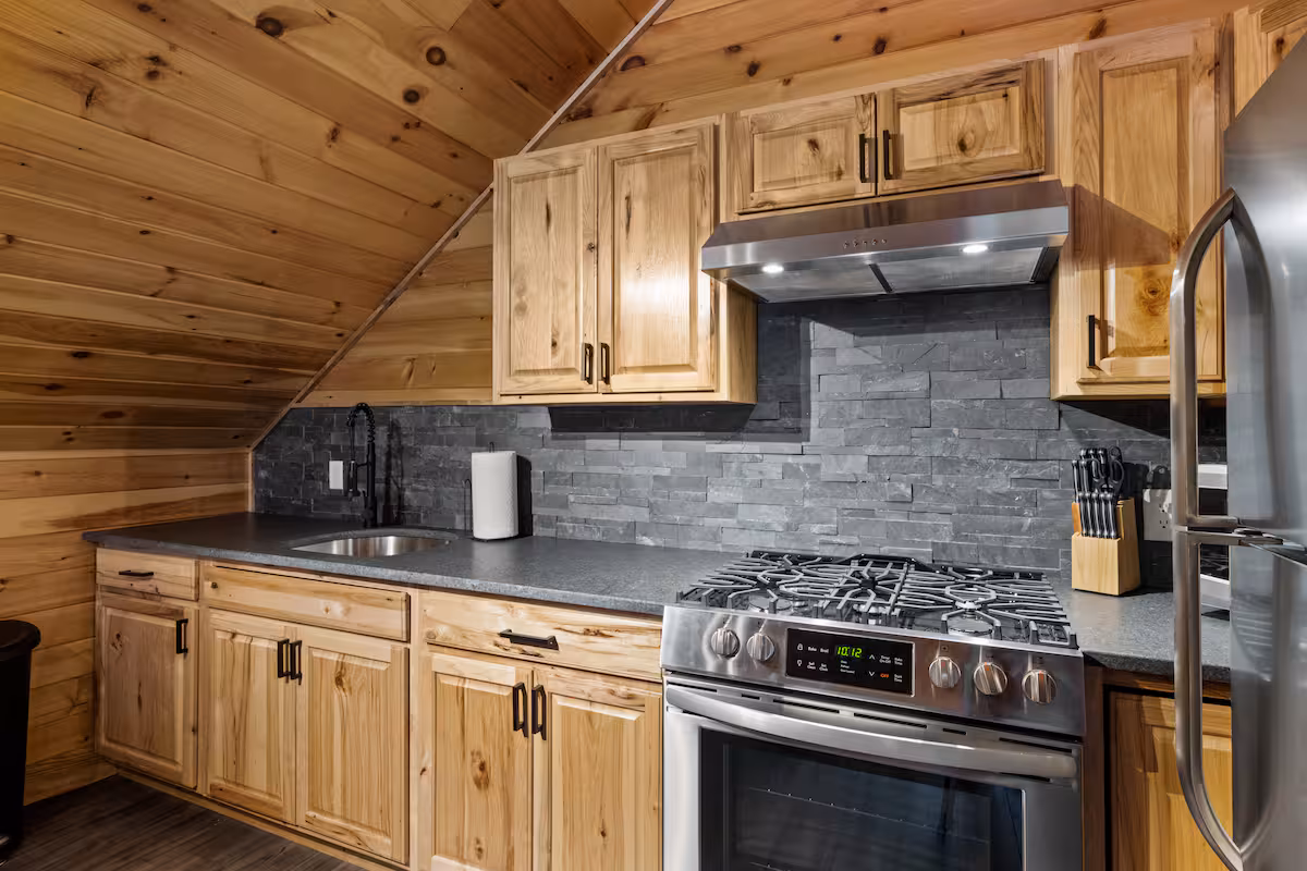 Full kitchen with stainless gas range, stone tile backsplash, and pine cabinetry